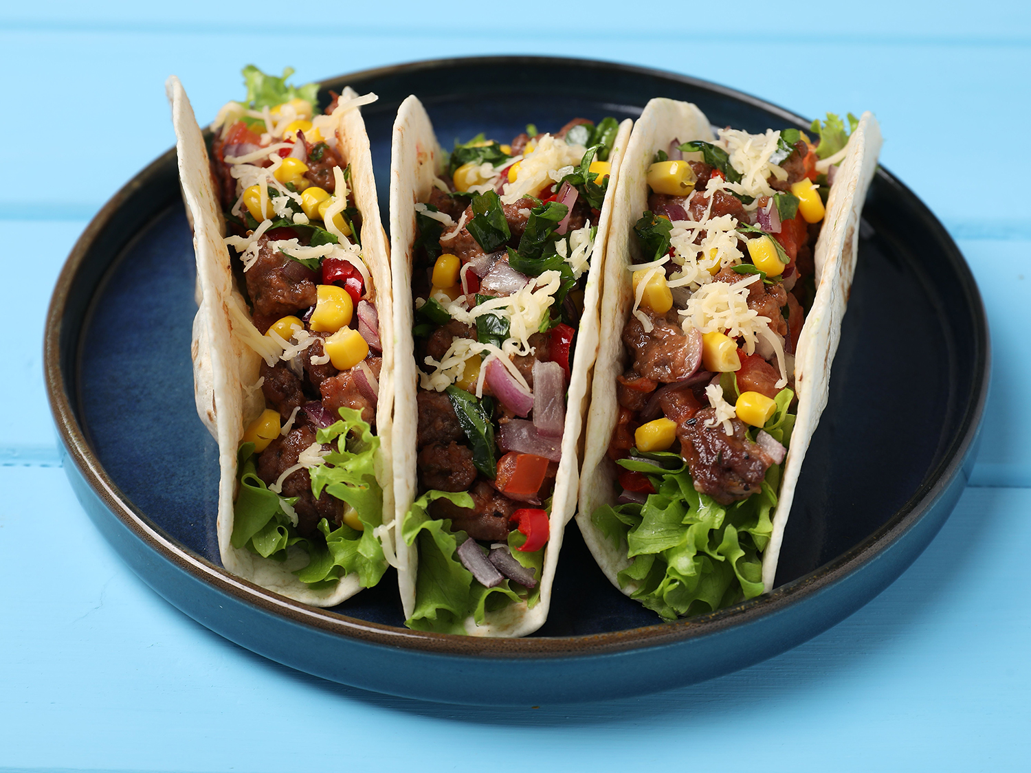 Delicious tacos with meat and vegetables on light blue table, cl
